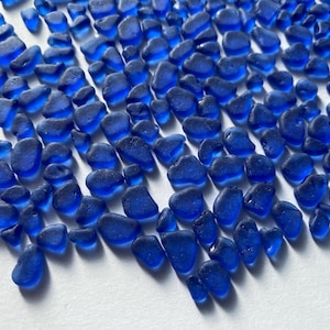 May include: A collection of small, smooth, cobalt blue sea glass pieces. The glass is translucent and has a variety of shapes and sizes.