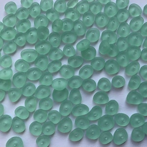 Op de afbeelding: Een verzameling lichtgroene glazen kralen met een matte afwerking. De kralen zijn gevormd als kleine, onregelmatige kiezelsteentjes met een gat in het midden.