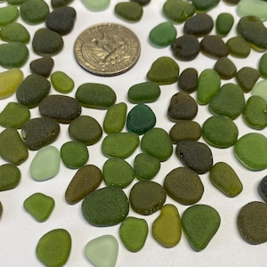 May include: A collection of smooth, green and brown sea glass stones. The sea glass is various shapes and sizes.