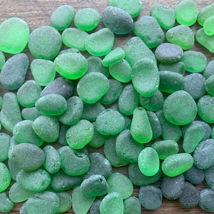 May include: A collection of smooth, green sea glass stones. The stones are various shapes and sizes, with a frosted, translucent appearance.