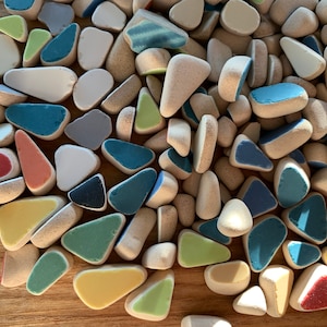 May include: A collection of small, irregularly shaped ceramic tiles in various colors, including blue, green, yellow, red, and white. The tiles are arranged in a random pattern, creating a visually appealing mosaic.