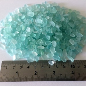 May include: A pile of light blue sea glass pieces, measured against a ruler, showing the size of the pieces.