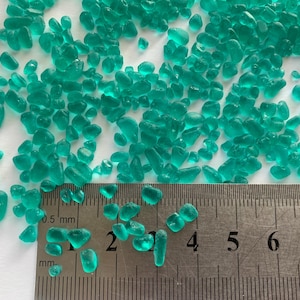May include: A close-up of a ruler measuring turquoise green glass beads. The ruler shows measurements in millimetres, with the largest bead measuring approximately 5 millimetres in diameter.