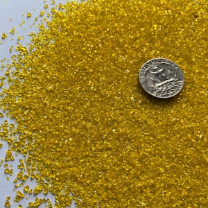 May include: A close-up of a pile of yellow glass glitter. A US quarter is included for scale.