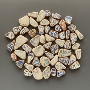 以下が含まれることがあります： 青と茶色の花柄が施された小さな白いセラミックタイルのコレクション。タイルは灰色の背景に円形に配置されています。