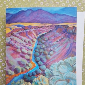 May include: A painting of a colorful landscape with a winding blue river flowing through a valley. The hills are painted in shades of purple, pink, and orange. The river is surrounded by green trees and bushes.
