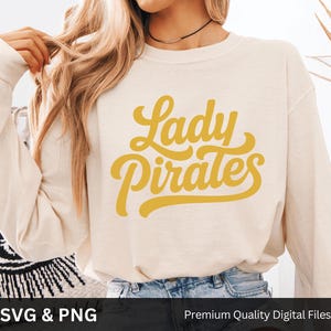 May include: Cream-colored long-sleeved sweatshirt with the text "Lady Pirates" in yellow script. The sweatshirt is made of a soft material and is suitable for casual wear. The image also includes the text "SVG & PNG" and "Premium Quality Digital Files".