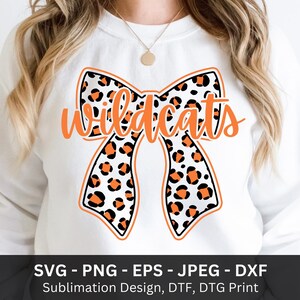 May include: White sweatshirt featuring an orange bow with a black outline and a leopard print pattern. The word "Wildcats" is written in orange script across the bow. Below the design are file type options.
