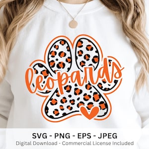 May include: White sweatshirt featuring an orange and black leopard paw print design with the word "Leopards" in orange script. The paw print has a black outline and a small orange heart. The bottom of the image includes the text "SVG - PNG - EPS - JPEG".