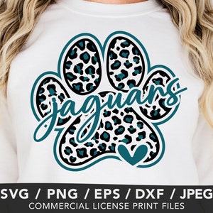 May include: A white sweatshirt featuring a large animal paw print graphic with a black and teal leopard spot pattern. The word jaguars is written in a teal script font across the centre, and a small teal heart is positioned at the bottom.