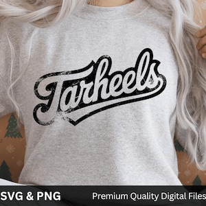May include: A light gray sweatshirt featuring the word "Tarheels" in a distressed black script font. The text is outlined in black and has a vintage, worn look. The sweatshirt is a casual style.
