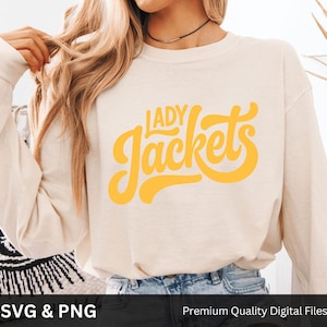 May include: Cream-colored long-sleeve sweatshirt with the words "LADY Jackets" in yellow script. The sweatshirt is paired with blue jeans. The bottom of the image has the text "SVG & PNG" and "Premium Quality Digital Files".
