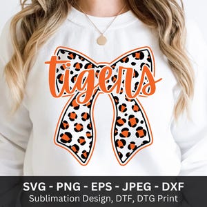 May include: White sweatshirt featuring a large bow design with a leopard print pattern in orange and black. The word "tigers" is written in orange script across the bow. The design is suitable for sublimation, DTF, and DTG printing.