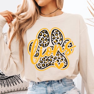 May include: Cream-colored sweatshirt featuring a large paw print design with a leopard print pattern. The word "Lions" is written in yellow script across the paw print. A small yellow heart is at the bottom.