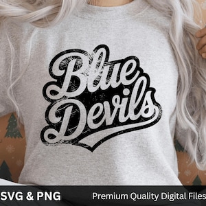 May include: A gray sweatshirt with the words "Blue Devils" in a distressed black and white design. The text is in a bold, stylized font with a decorative border. The sweatshirt is a neutral color, suitable for various occasions.