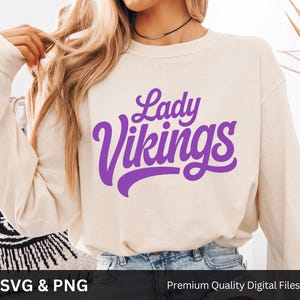 Puede incluir: Sudadera color crema con las palabras "Lady Vikings" en escritura púrpura. La parte superior de manga larga está hecha de un material suave. La imagen también incluye el texto "SVG & PNG" y "Premium Quality Digital Files".