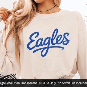 May include: Cream-colored long-sleeve sweatshirt with the word "Eagles" in blue script across the front. The text has a stitched appearance. The sweatshirt is a neutral color, suitable for various outfits.