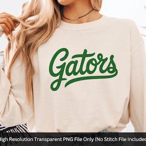 May include: Cream-colored sweatshirt with the word "Gators" in green script across the front. The text has a textured, stitched appearance. The image is a close-up of the shirt.