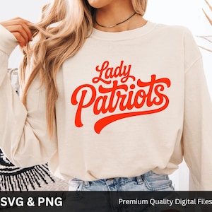 May include: Cream-colored long-sleeve sweatshirt with the words "Lady Patriots" in bright red script. The sweatshirt is made of a soft material and is suitable for casual wear. The image also includes the text "SVG & PNG" and "Premium Quality Digital Files".