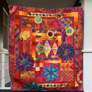 Puede incluir: Una colcha colorida con un patrón geométrico que presenta una variedad de diseños florales en tonos de rojo, naranja, amarillo, azul y verde.