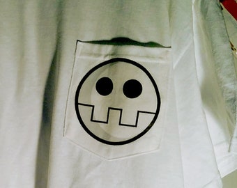 Könnte beinhalten: Weißes T-Shirt mit einer Tasche mit einem schwarzen und weißen Totenkopf-Motiv.