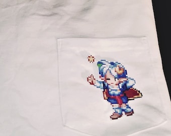 May include: White t-shirt with a pocket featuring a pixelated character design. The character is blue, red, and white and is holding a star.