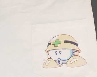 Könnte beinhalten: Weißes T-Shirt mit einer Tasche, die einen Comic-Charakter zeigt, der einen gelben Helm mit einem grünen Kreuz trägt.