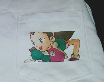 Könnte beinhalten: Weißes T-Shirt mit einer Tasche, die ein Cartoon-Bild eines Mädchens mit braunen Haaren, grüner und rosa Kleidung und einem gelben Ohrring zeigt.