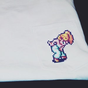 May include: White long-sleeve t-shirt with a pocket featuring a pixelated image of a character from a video game.