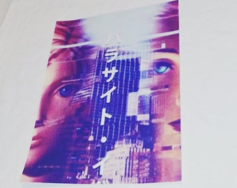 Op de afbeelding: Wit t-shirt met een grafische print met een gezicht en Japanse tekst. De afbeelding gebruikt paarse, roze en blauwe tinten. Het shirt is gemaakt van een zacht, comfortabel materiaal.