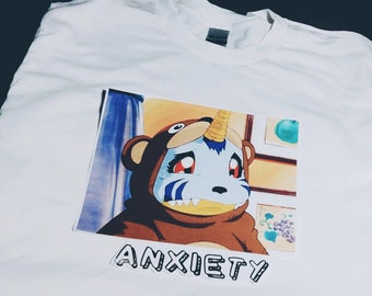 May include: White t-shirt with a cartoon image of a blue and brown creature with a horn. The text "ANXIETY" is printed below the image.
