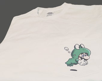 May include: White t-shirt with a green cartoon character wearing a frog costume. The character is swimming and has a surprised expression on its face.