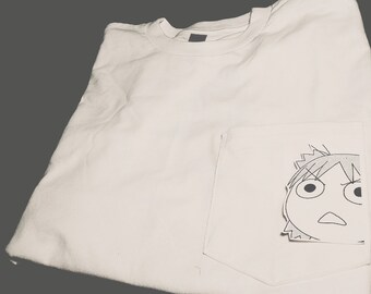 May include: White t-shirt with a pocket featuring a black and white cartoon drawing of a character with large eyes and a surprised expression.