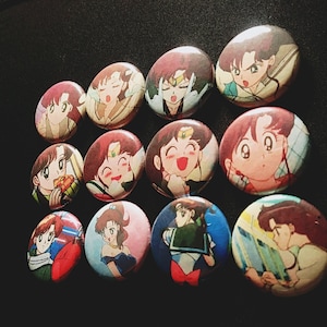 May include: A collection of twelve round, colorful anime character buttons. The buttons feature various characters with different expressions and poses.
