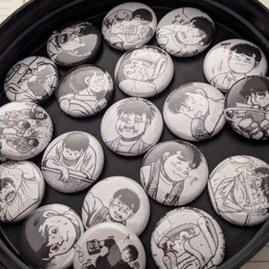 May include: A collection of 18 black and white round pinback buttons featuring various anime characters. The buttons are arranged in a circle on a black surface.