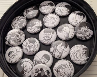 Op de afbeelding: Een verzameling van 18 ronde zwart-witte pinback-knoppen met verschillende anime-personages. De knoppen zijn in een cirkel op een zwart oppervlak gerangschikt.