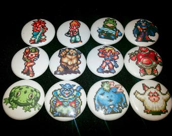 May include: Twelve round, white, button pins with colorful pixelated images of characters and creatures. The pins feature a variety of characters, including a frog, a knight, a warrior, a creature with a crown, and a creature with a red shell.