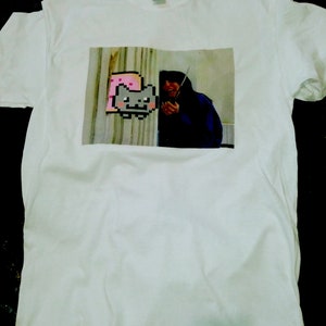May include: White t-shirt with a printed image of a person holding a knife and a pixelated cat wearing a pink slice of bread.