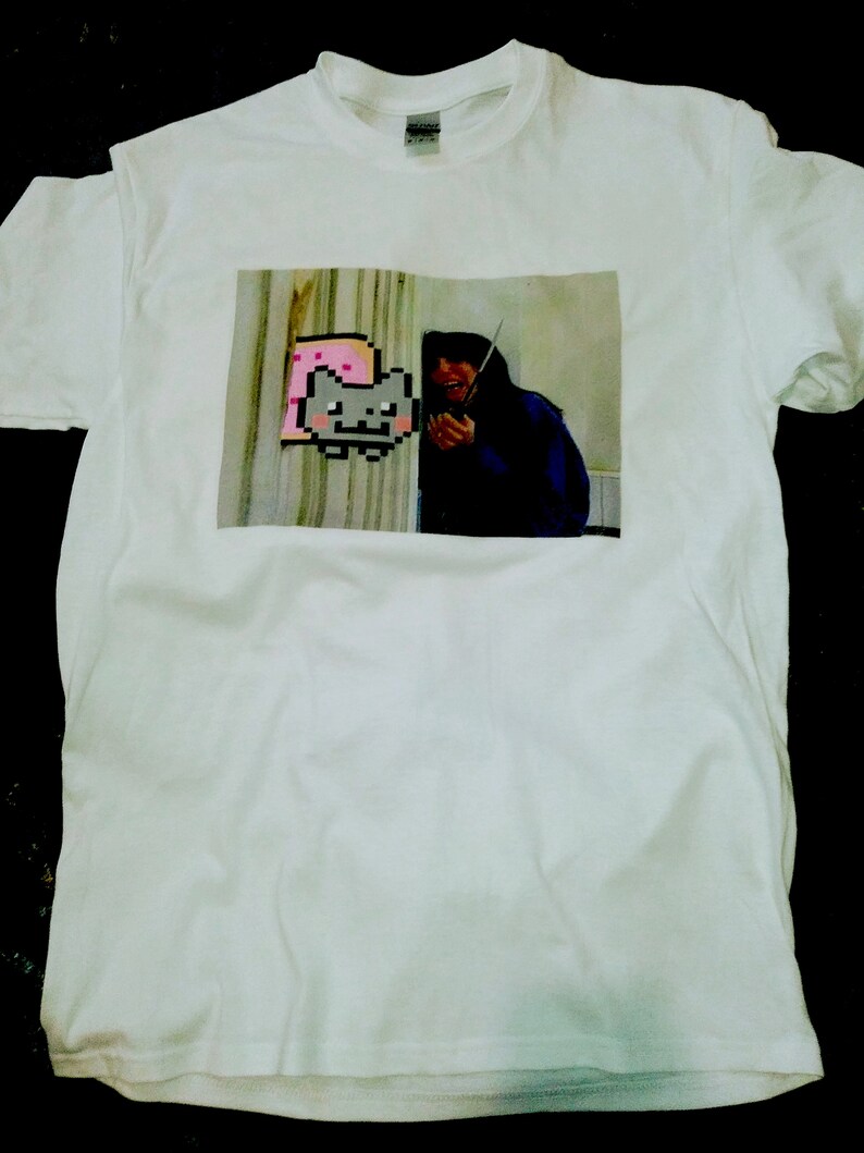 May include: White t-shirt with a printed image of a person holding a knife and a pixelated cat wearing a pink slice of bread.