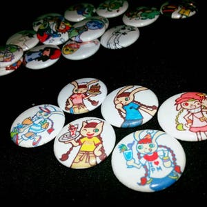 May include: A collection of white, oval-shaped buttons with colorful cartoon illustrations. The designs feature various characters, including rabbits and other figures, in different outfits and poses. The buttons are scattered on a black surface.
