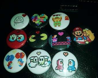 May include: A set of 10 round, colorful, pixelated buttons featuring characters from popular video games. The buttons are approximately 1 inch in diameter and have a white background with black outlines. The characters include Mario, Luigi, Pac-Man, Donkey Kong, and Link.