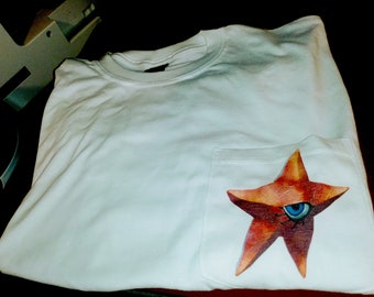 Könnte beinhalten: Weißes T-Shirt mit einer Tasche, die mit einem roten und orangefarbenen Seestern mit einem blauen Auge verziert ist.