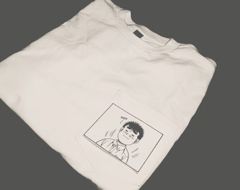 May include: White t-shirt with a pocket featuring a black and white cartoon illustration of a person with the word "Sniff" above them.