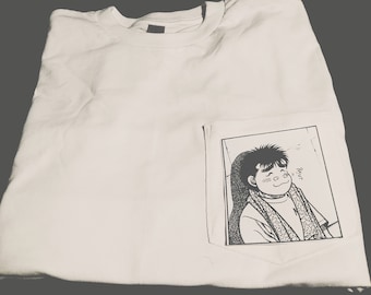 Op de afbeelding: Wit T-shirt met een zwart-witte grafische print van een cartoonfiguur in een zak. Het personage glimlacht en heeft een sjaal om zijn nek. De tekst "R.Y.U.P." is boven het personage gedrukt.