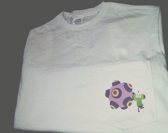 Op de afbeelding: Wit T-shirt met een zak met daarop een cartoonfiguur dat een paarse en gele bol vasthoudt met rode en witte cirkels.