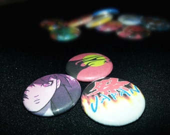 May include: Three round pinback buttons with different designs. The first button has a red background with a black silhouette of a tree and a yellow circle in the center. The second button has a purple background with a cartoon drawing of a woman with long purple hair. The third button has a white background with a red and yellow flame design and the word "JAPAN" in blue letters.