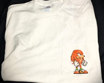 Op de afbeelding: Wit T-shirt met een rode en groene gepixelde afbeelding van Knuckles the Echidna uit de Sonic the Hedgehog-videogameserie op de zak.