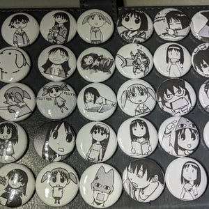 May include: A collection of 36 round black and white buttons featuring various cartoon characters. The buttons are arranged in a grid pattern on a black surface.