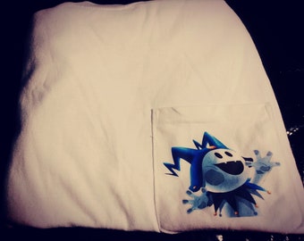 Könnte beinhalten: Weißes T-Shirt mit einer Tasche, die eine Cartoonfigur mit blauem und weißem Farbschema zeigt. Die Figur hat einen Narrenhut und lächelt mit ausgestreckten Armen. Das Shirt ist aus einem weichen Material.