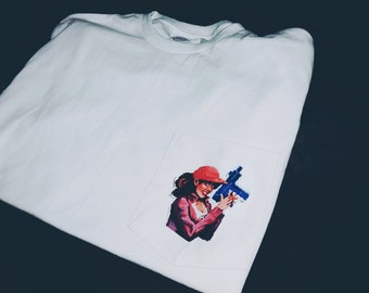 Könnte beinhalten: Weißes Langarm-T-Shirt mit einer Tasche, die ein pixeliges Bild einer Frau mit roter Kappe und rosa Jacke mit einer blauen Waffe zeigt. Das Shirt ist aus weißem Stoff.